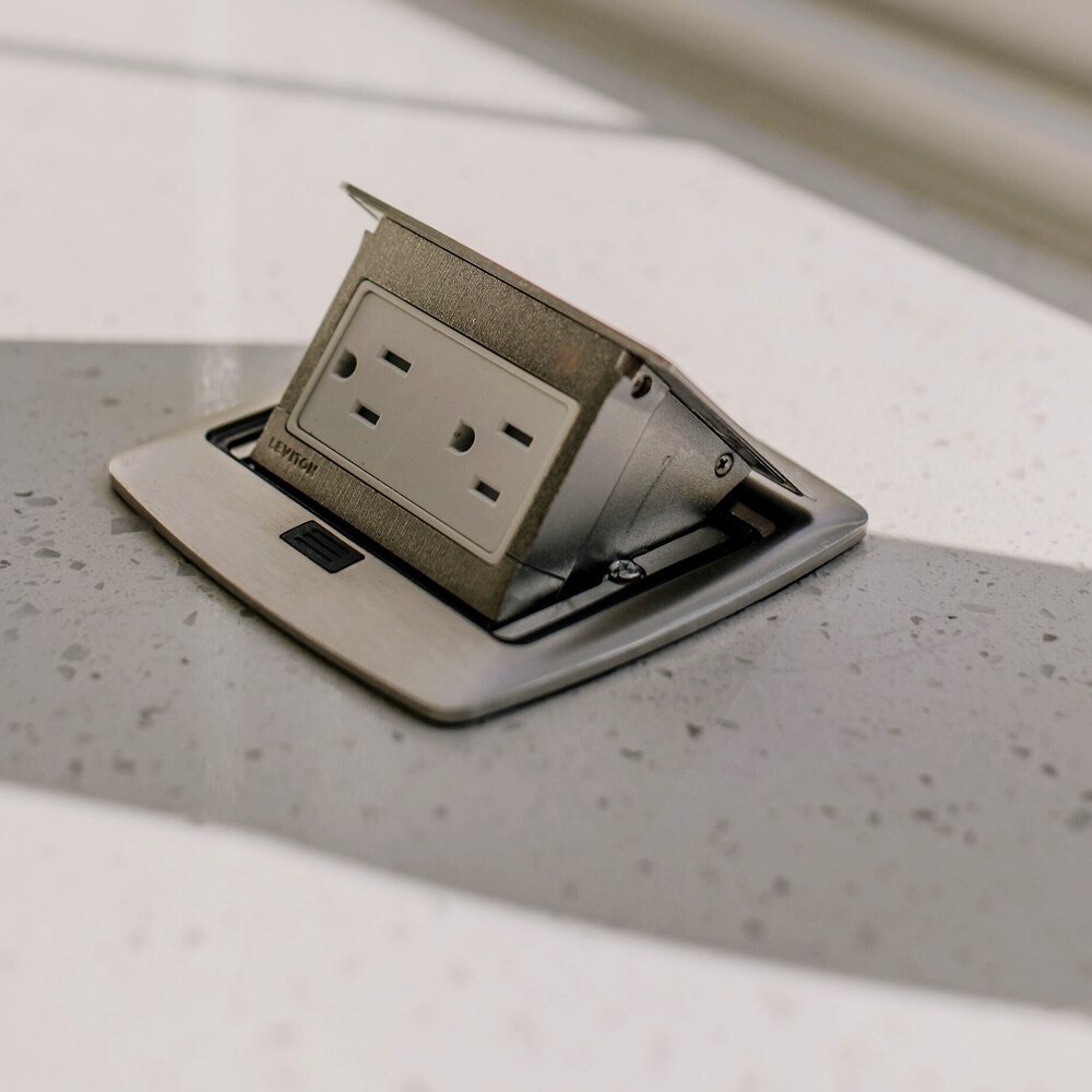 MSI Iced White quartz countertop with fine gray specks and a brushed metal pop-up electrical outlet installed in the surface.
