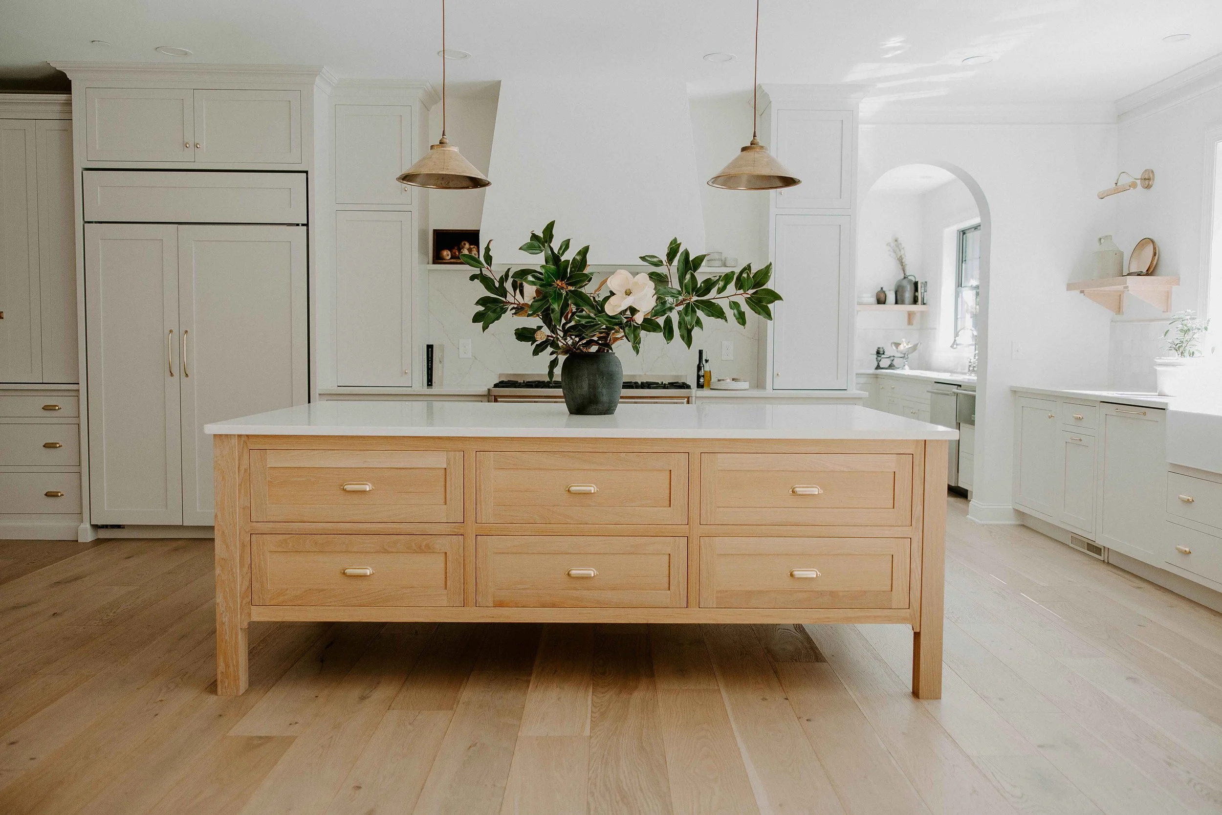 Bright remodeled kitchen with a custom wood island, white cabinetry, brass hardware, and pendant lighting.