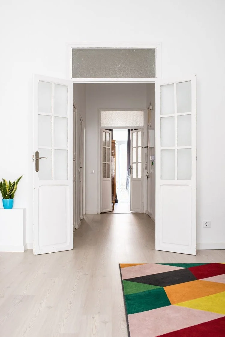 Light wood-look vinyl or linoleum flooring extending through a bright hallway with white glass-pane doors and a geometric rug.