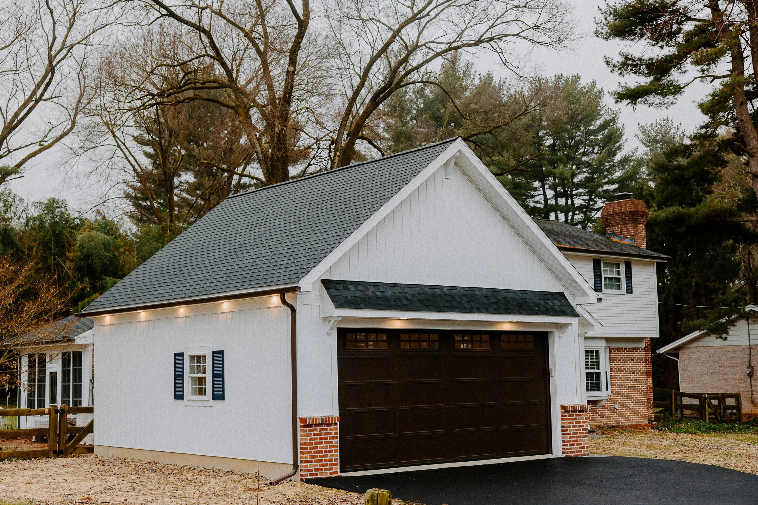 General contracting project featuring a detached garage and home addition with white siding, a dark roof, and brick accents.