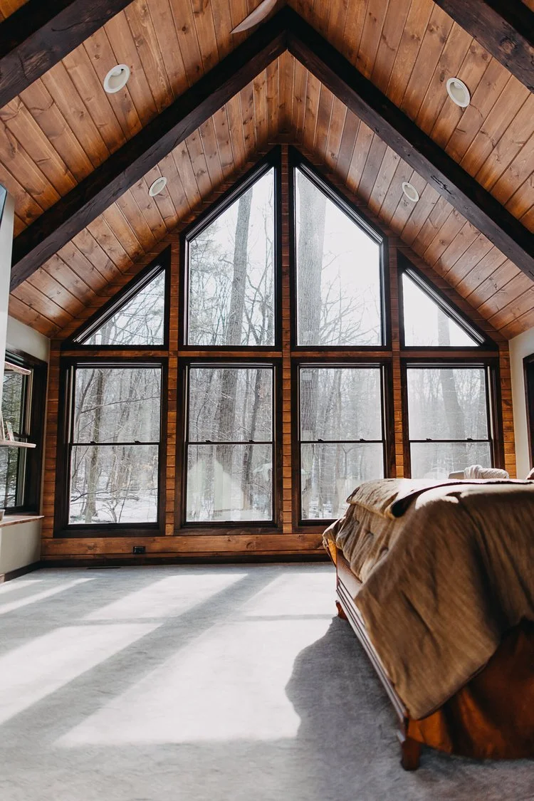 Plush carpet flooring throughout a bedroom with large windows, a vaulted wood-paneled ceiling, and exposed beams.