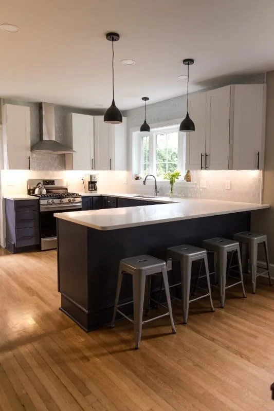 A two-tone kitchen combines stainless steel appliances, under-cabinet lighting, white quartz countertops, and warm hardwood flooring.