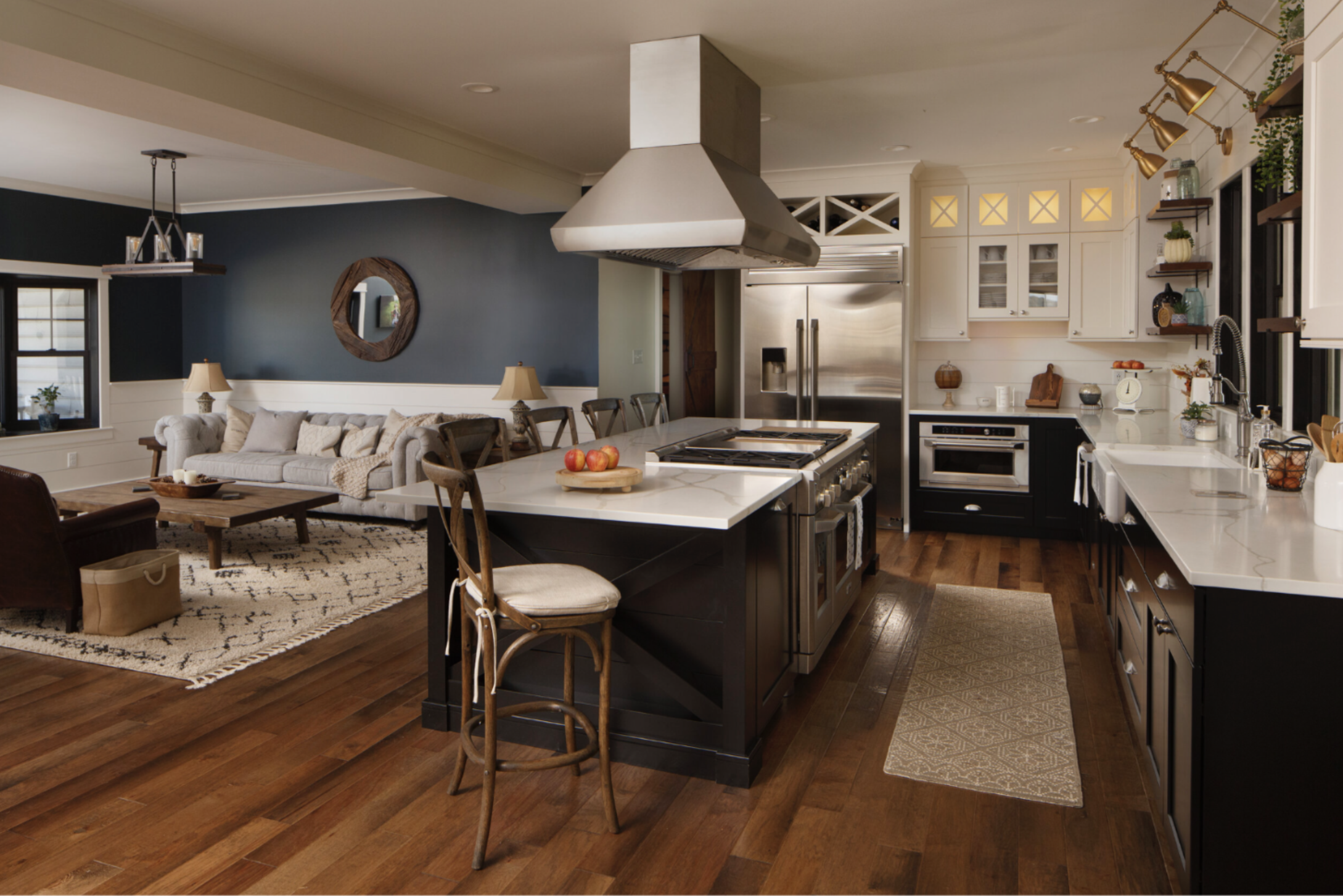 Spacious open-concept interior connecting a kitchen with a dark island and white quartz countertop to a living room with a gray sofa.