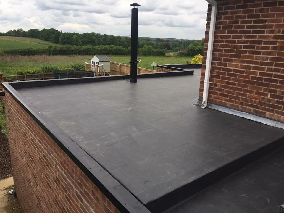 Flat residential roof covered with black EPDM rubber membrane and surrounded by brick walls.