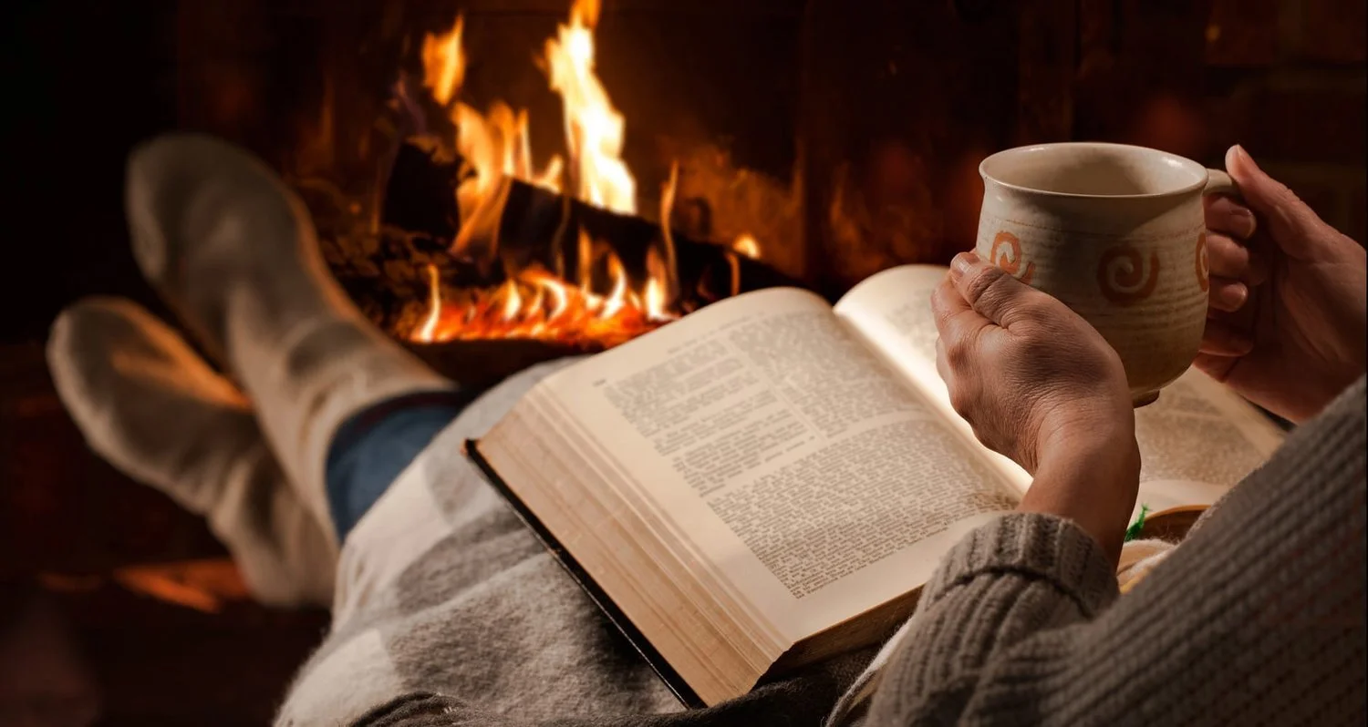 Cozy scene of a person enjoying a book and warm drink beside a crackling fireplace as part of a relaxing home routine.
