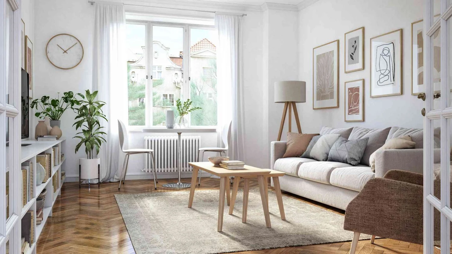 Bright living room with chevron hardwood flooring, a light gray sofa, wooden coffee tables, plants, and botanical artwork.