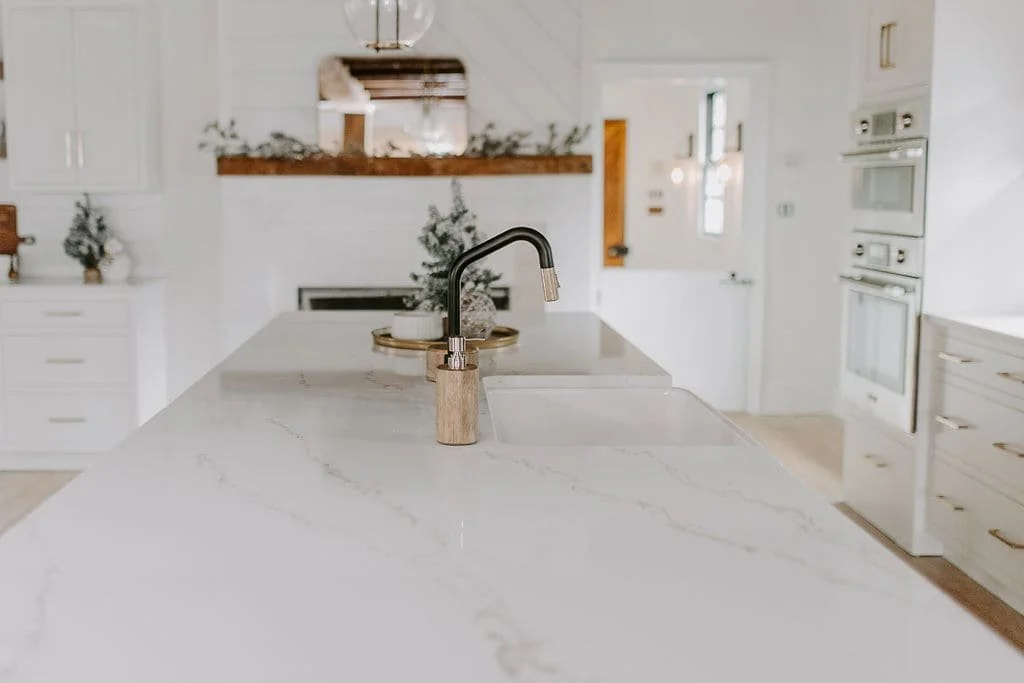 Open-concept kitchen with white quartz countertops, a large island, white cabinetry, stainless steel appliances, and a shiplap fireplace.