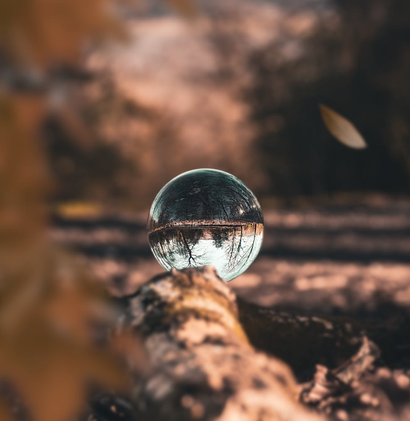 Crystal glass sphere balanced on a textured surface with an inverted reflection of trees and an autumn landscape.