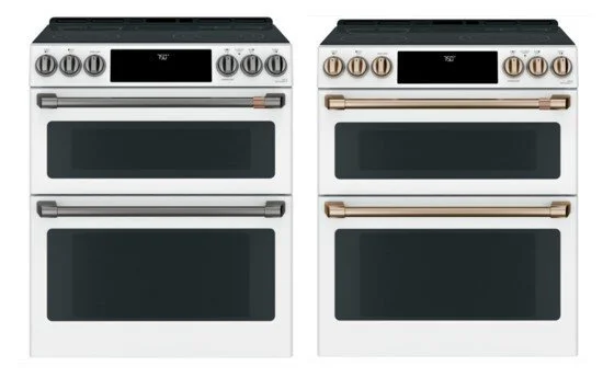 Two white double-oven electric ranges displayed side by side with digital controls and contrasting bronze and copper hardware options.