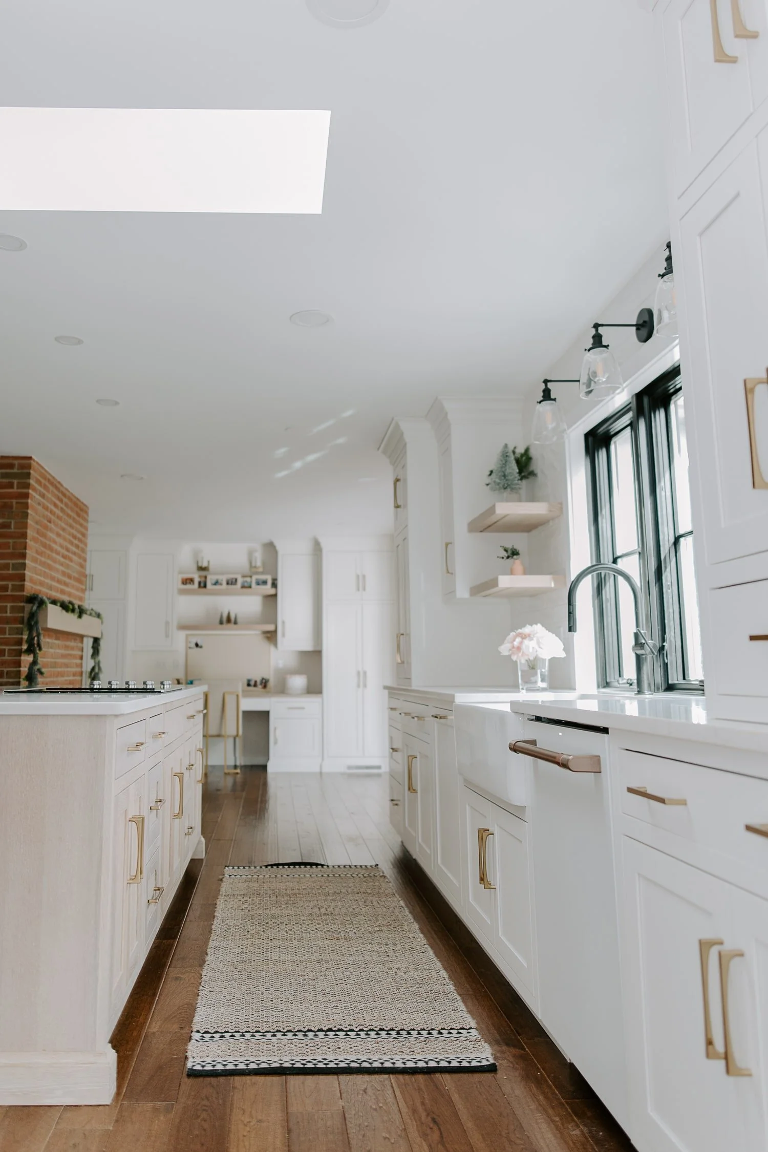 A bright white kitchen features shaker-style cabinets, brass hardware, rich hardwood floors, and a long central island.