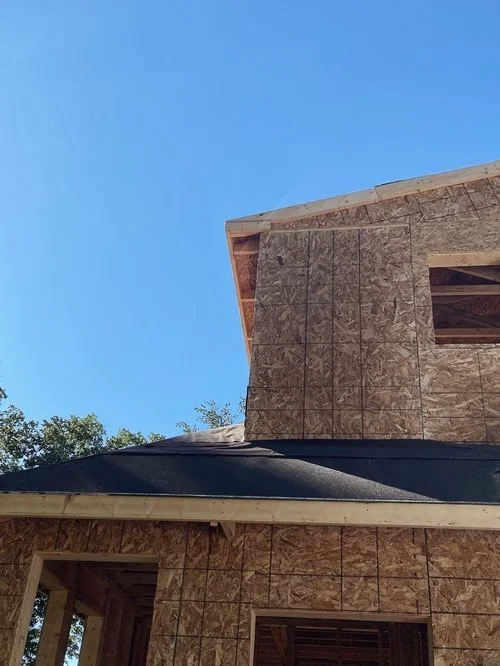 Residential home addition under construction with newly framed wood walls, OSB sheathing, window openings, and a pitched roof.