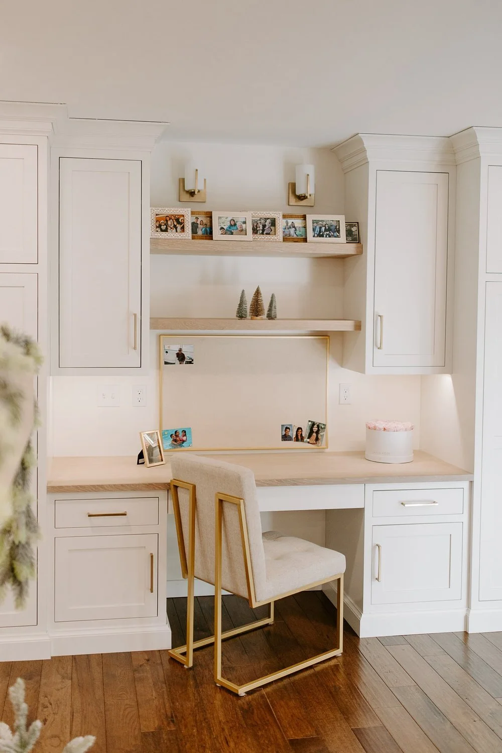 Modern built-in workspace with white cabinetry, warm wood accents, brass hardware, display shelves, and a geometric-frame chair.