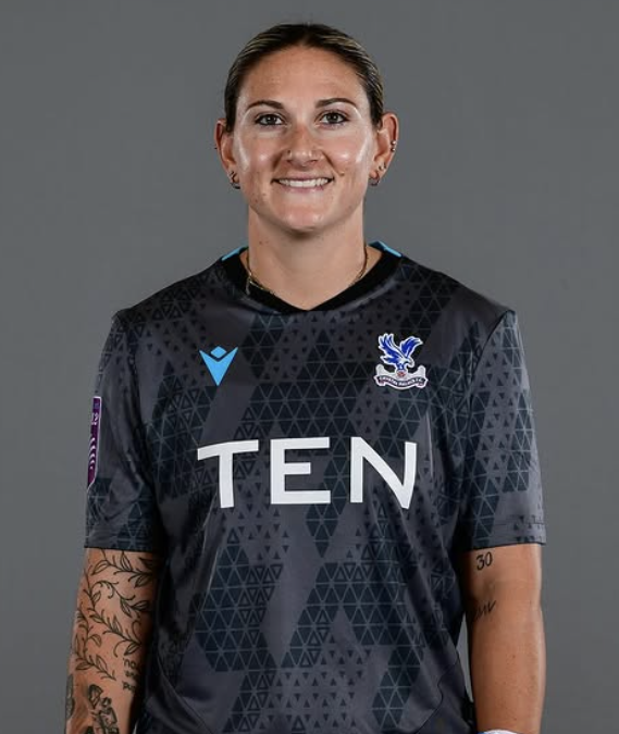 A young woman with dark hair tied back, wearing a bright green sports jersey, standing outdoors with a blurred background.