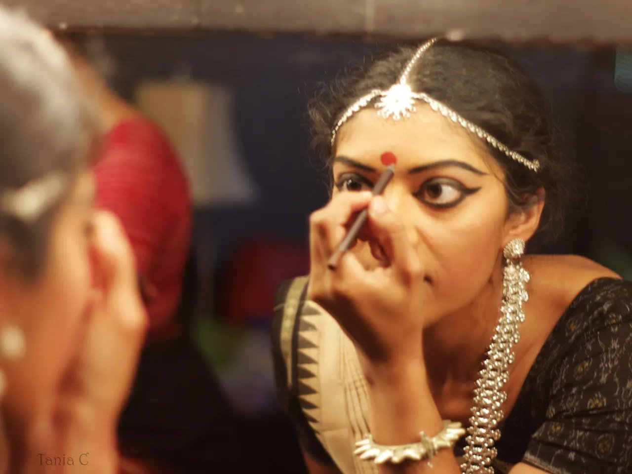 An odissi dancer drawing out precise makeup lines