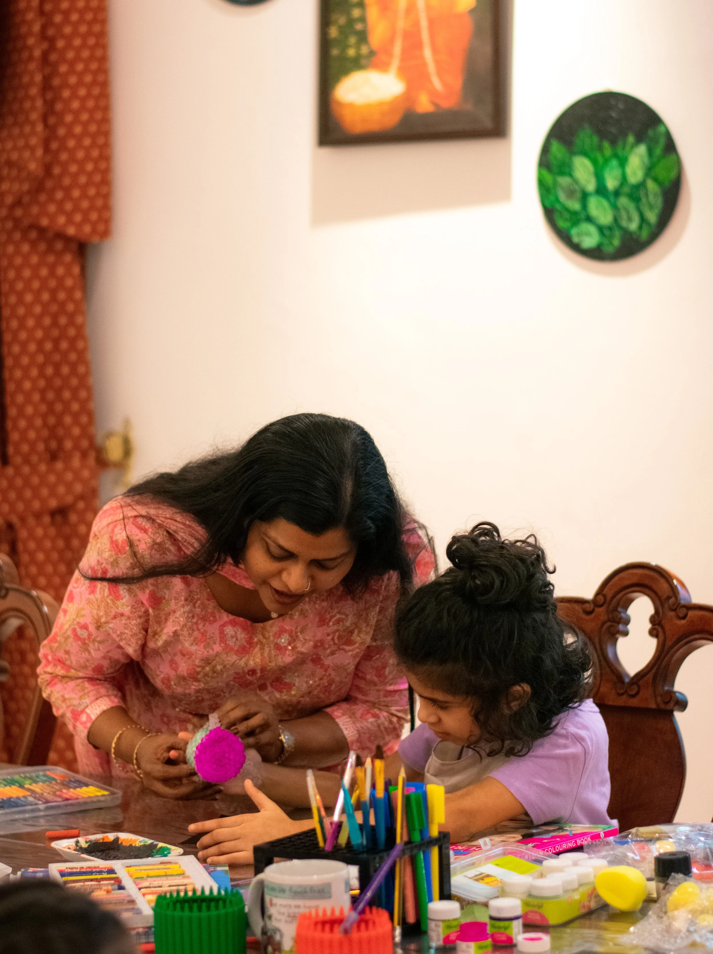Woman and girl engaged in arts and crafts at a table with colorful supplies.