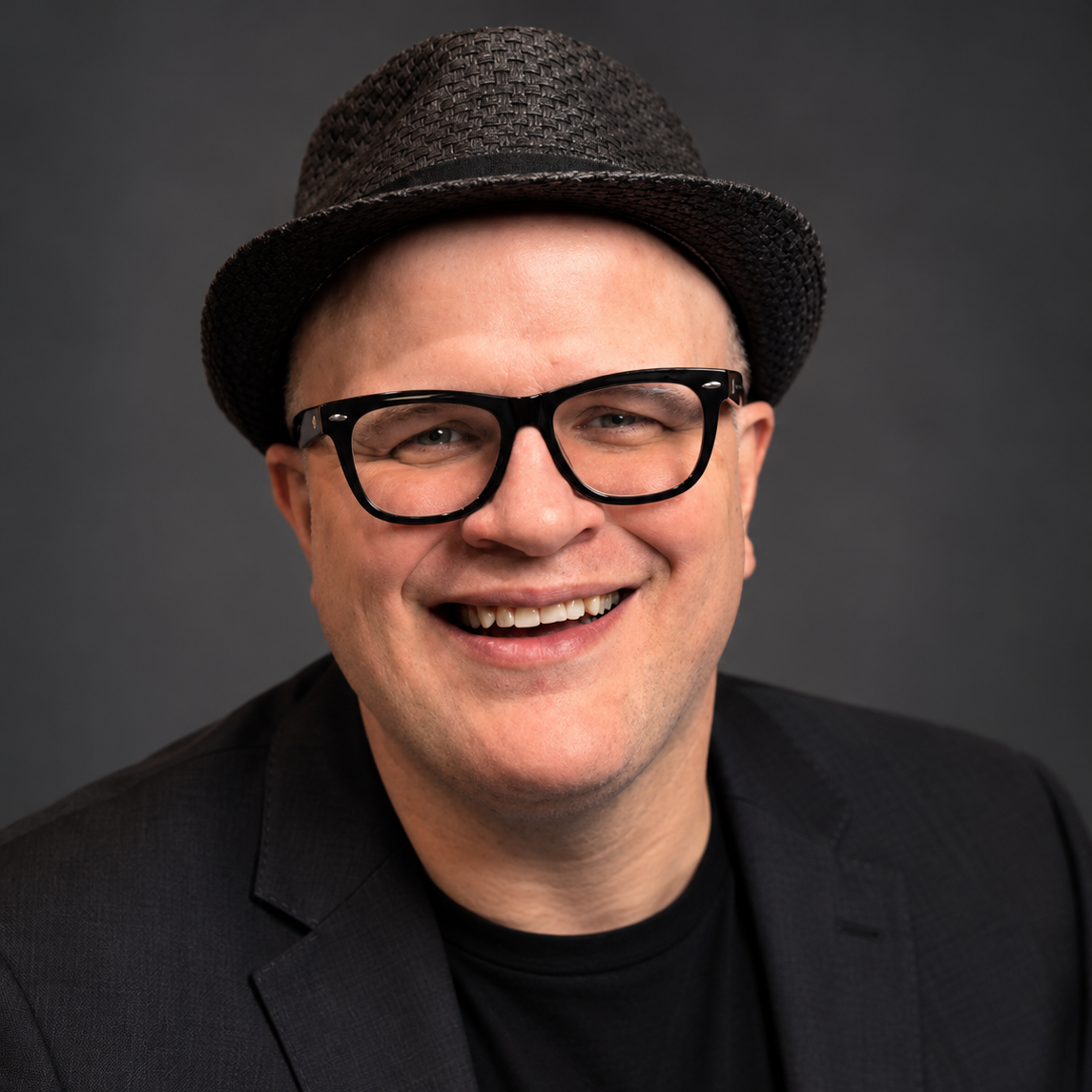 Adam Reader, the Professor of Rock, smiling portrait wearing glasses and a hat
