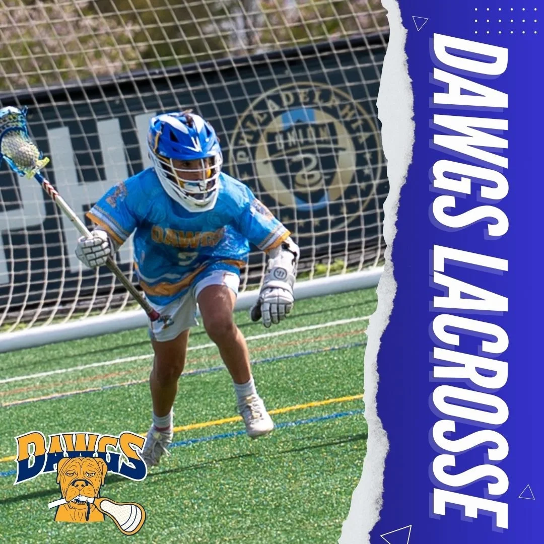 Young lacrosse goalie wearing a blue helmet and jersey, crouched in front of goal on artificial turf field.