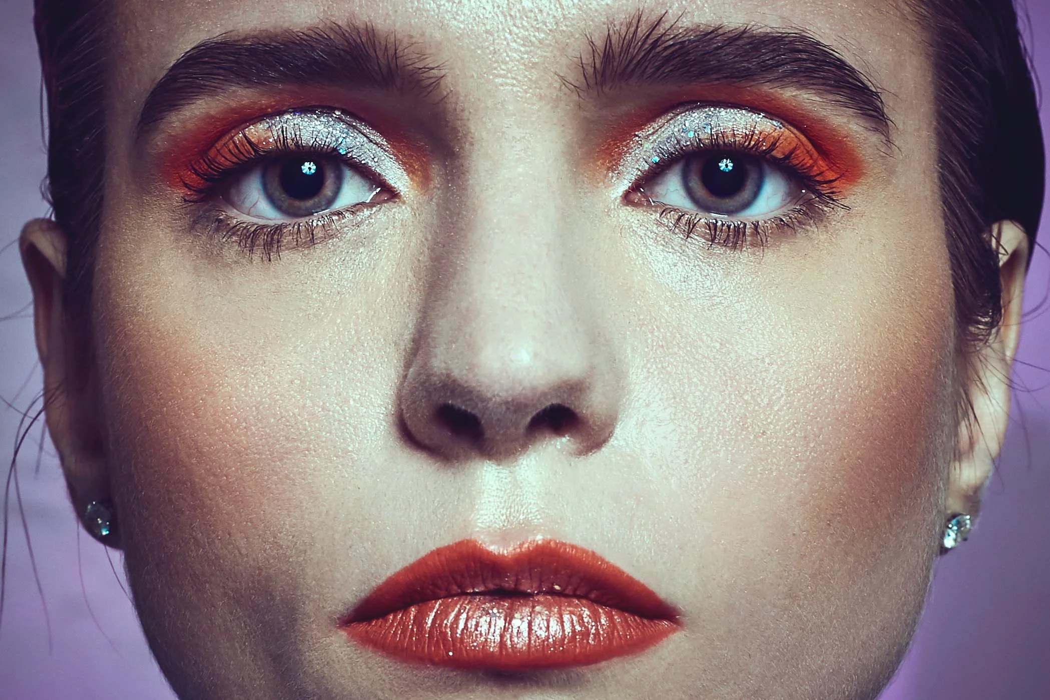 Close-up of a woman's face with colorful makeup, including shimmering eye shadow, bold lipstick, and earrings.