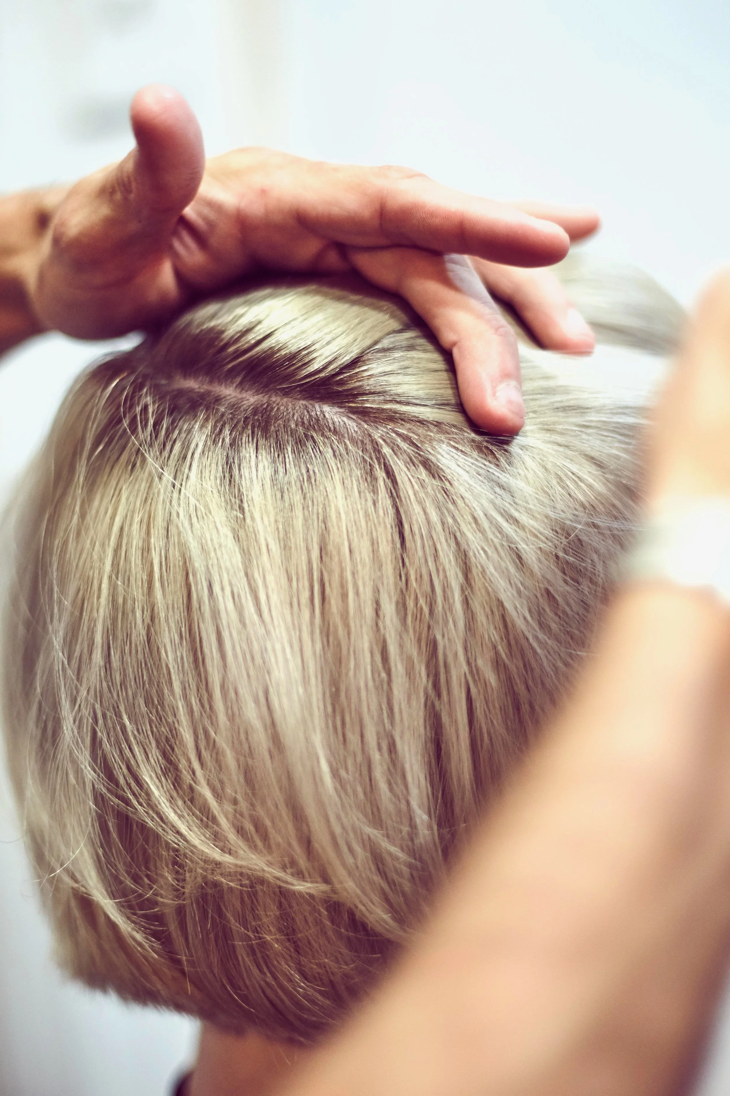 Close-up of a person receiving a scalp massage from a therapist, focusing on the top of their short, blonde hair.