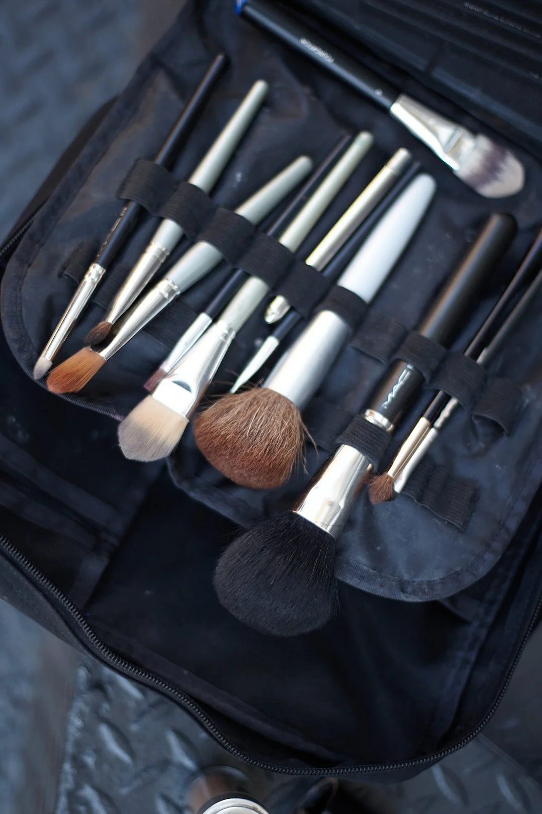 Set of makeup brushes in a black carrying case, with various sizes and shapes, some with black, white, or brown bristles.