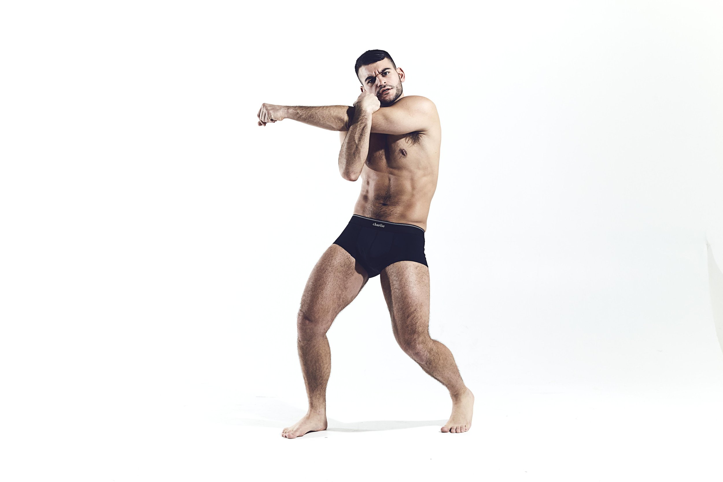 A shirtless man in black underwear stretching against a plain white background.