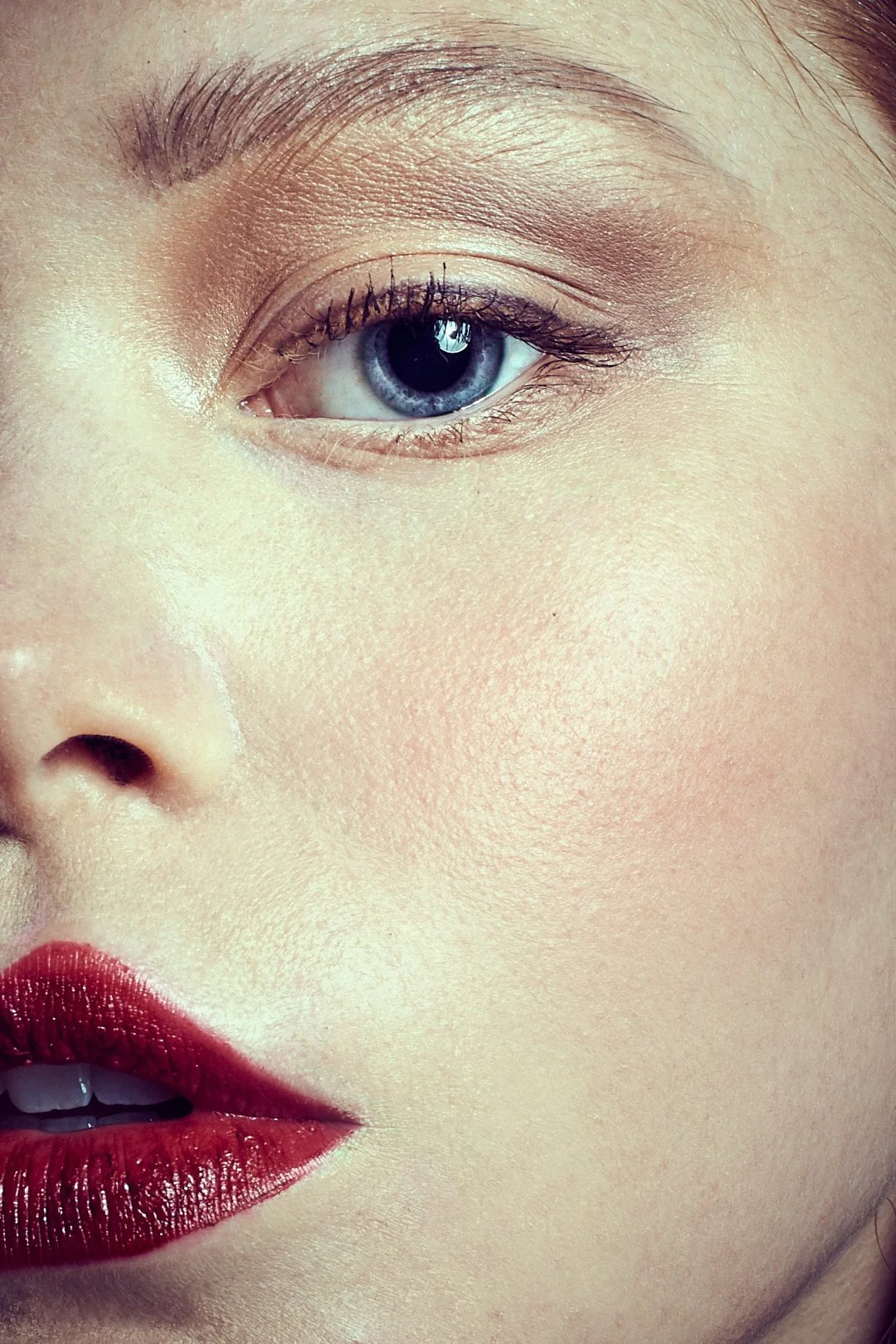 Close-up of a woman's face showing her eye, part of her nose, and her lips with red lipstick.