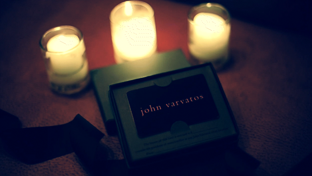 Gift card labeled 'John Varvatos' with three lit candles nearby.