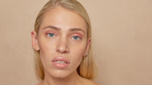Person with blonde hair and pink eye makeup, looking directly at camera against a neutral background.