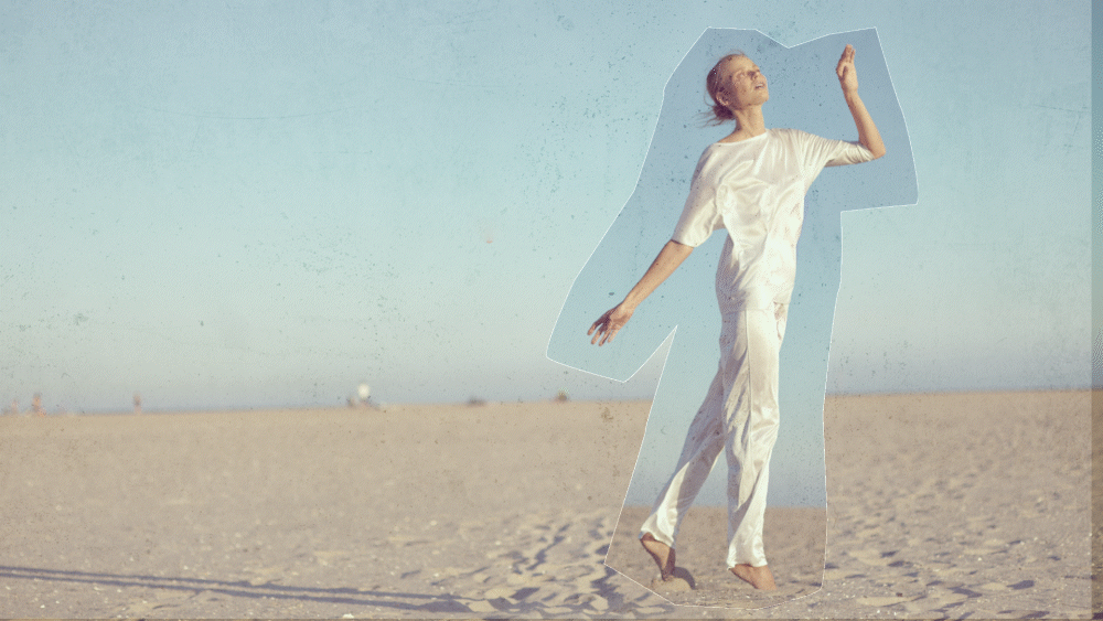 Person in white outfit striking a pose on a beach with a clear sky.