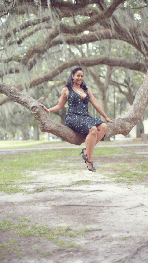 Woman in black dress sitting on tree branch in a park