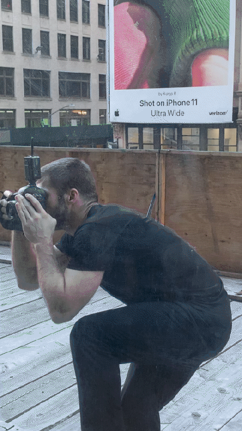 Person squatting with camera photographing a billboard for iPhone 11 Ultra Wide.
