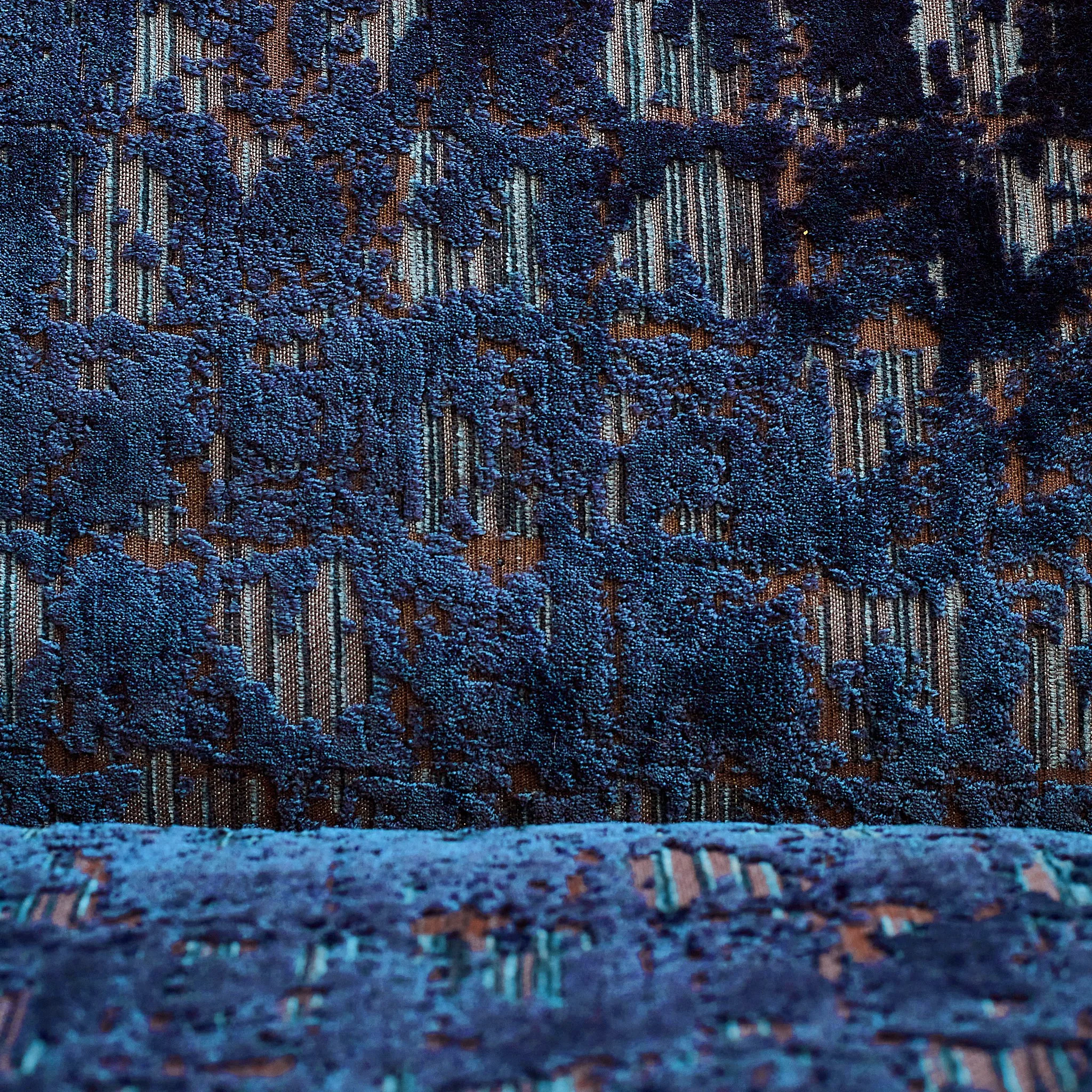 Close-up of a blue textured fabric with a pattern of stripes and raised floral designs.