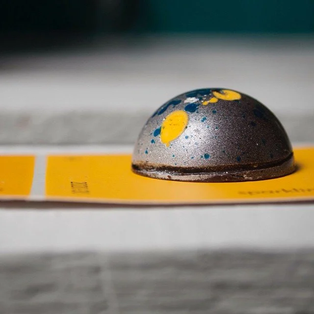 A close-up of a metal disc with blue and yellow paint splatters resting on a yellow surface.