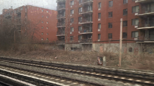 View from a moving train showing railway tracks and adjacent buildings.