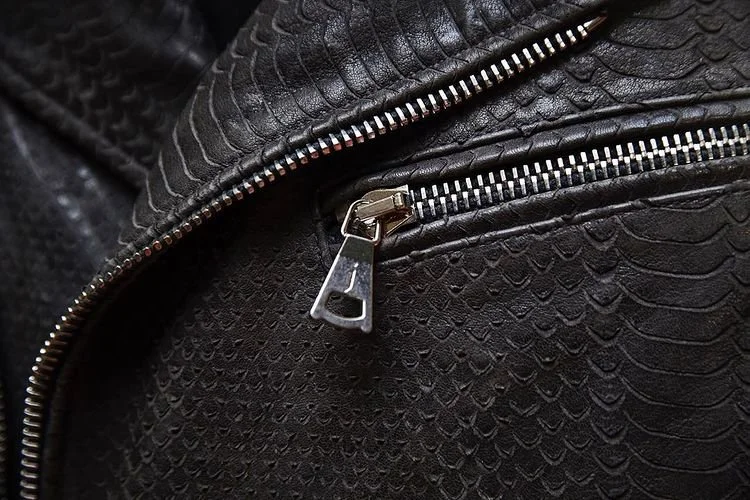 Close-up of a black leather surface with a textured pattern, featuring a silver zipper.