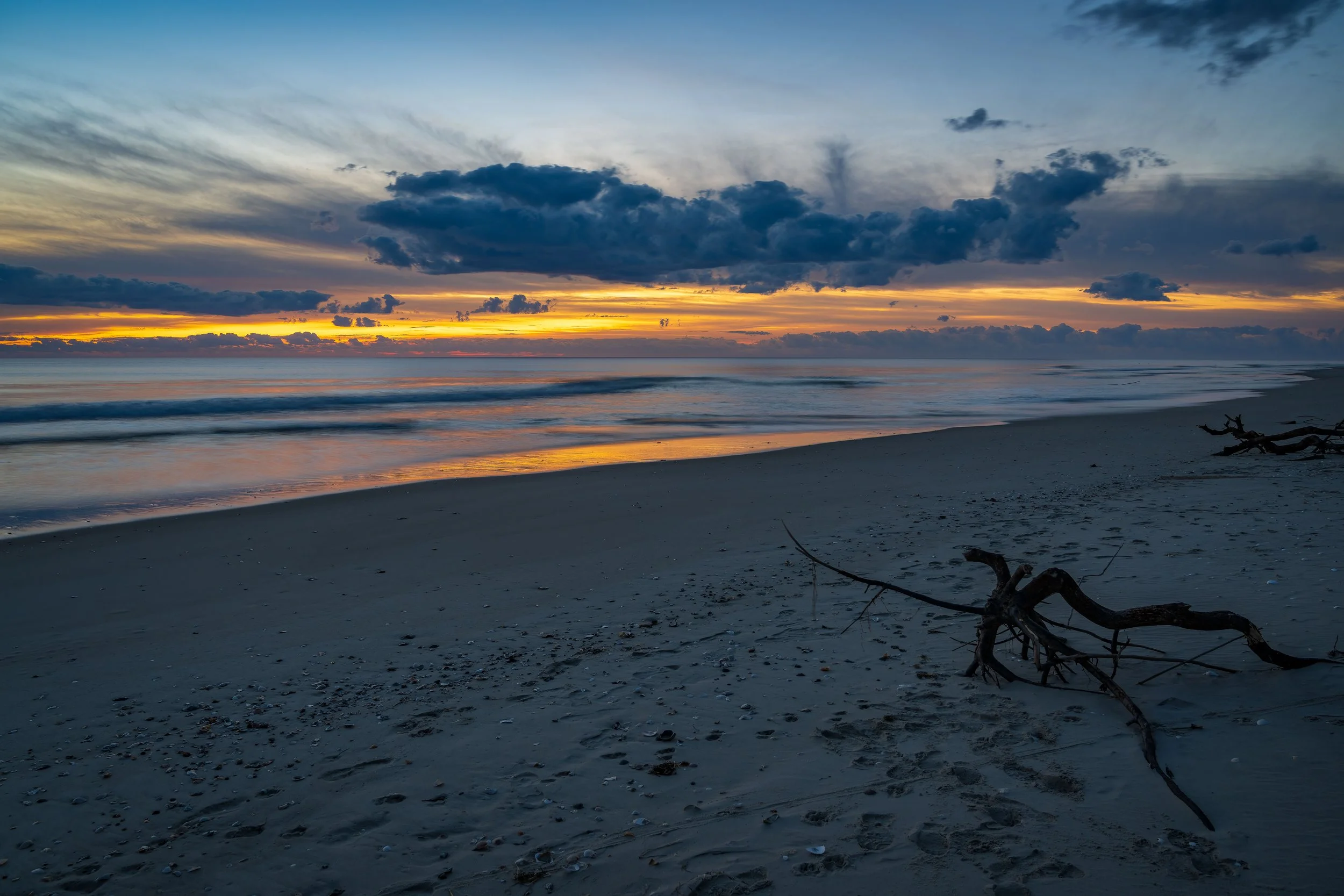 This photo captures a stunning sunrise over the Atlantic Ocean near Pea Island Wildlife Refuge in North Carolina. The scene is viewed from the beach, with the ocean stretching out into the distance and the sky lit up with vibrant hues of orange, pink