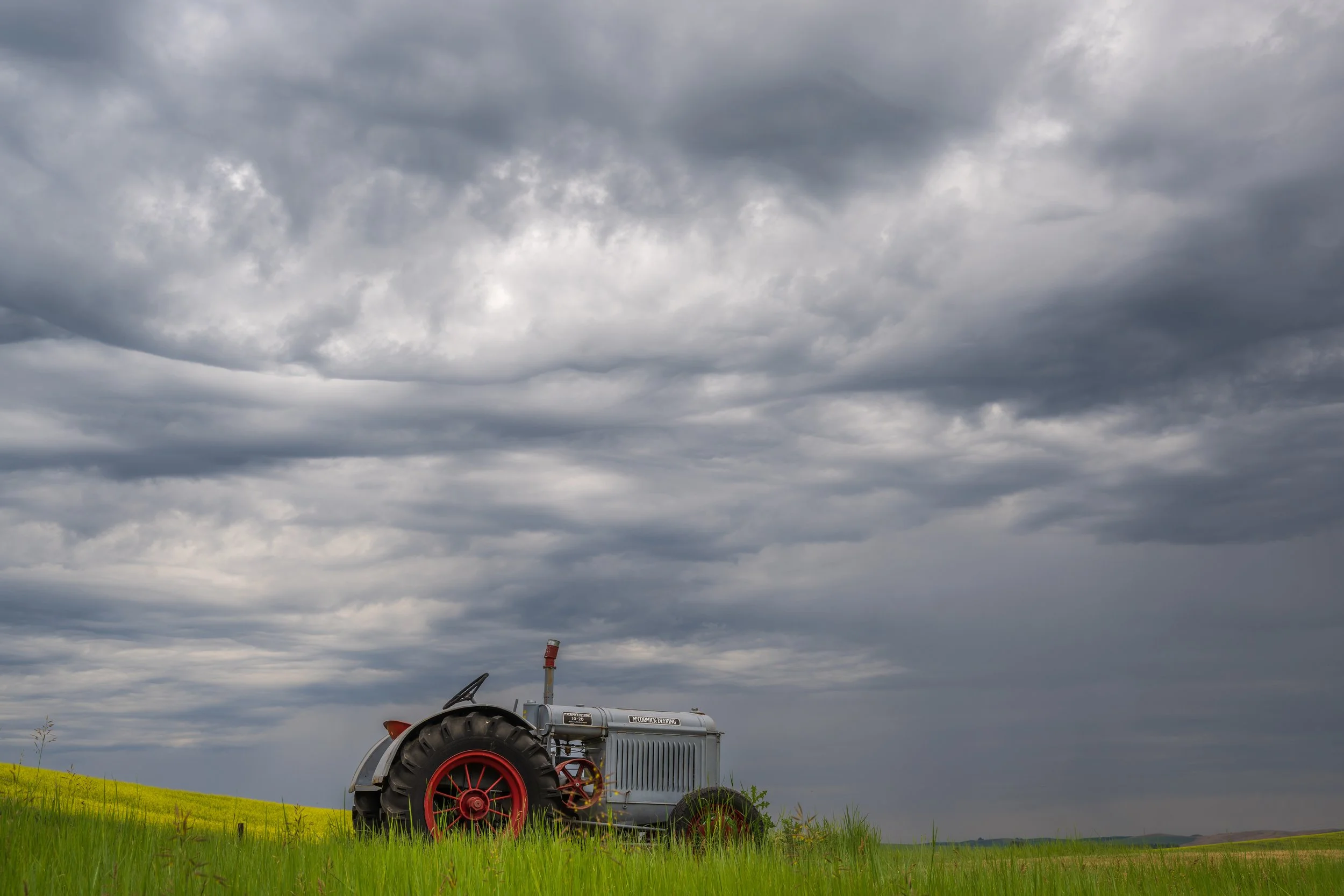Out of commission tractor with budding canola fields near Colfax, Washington.