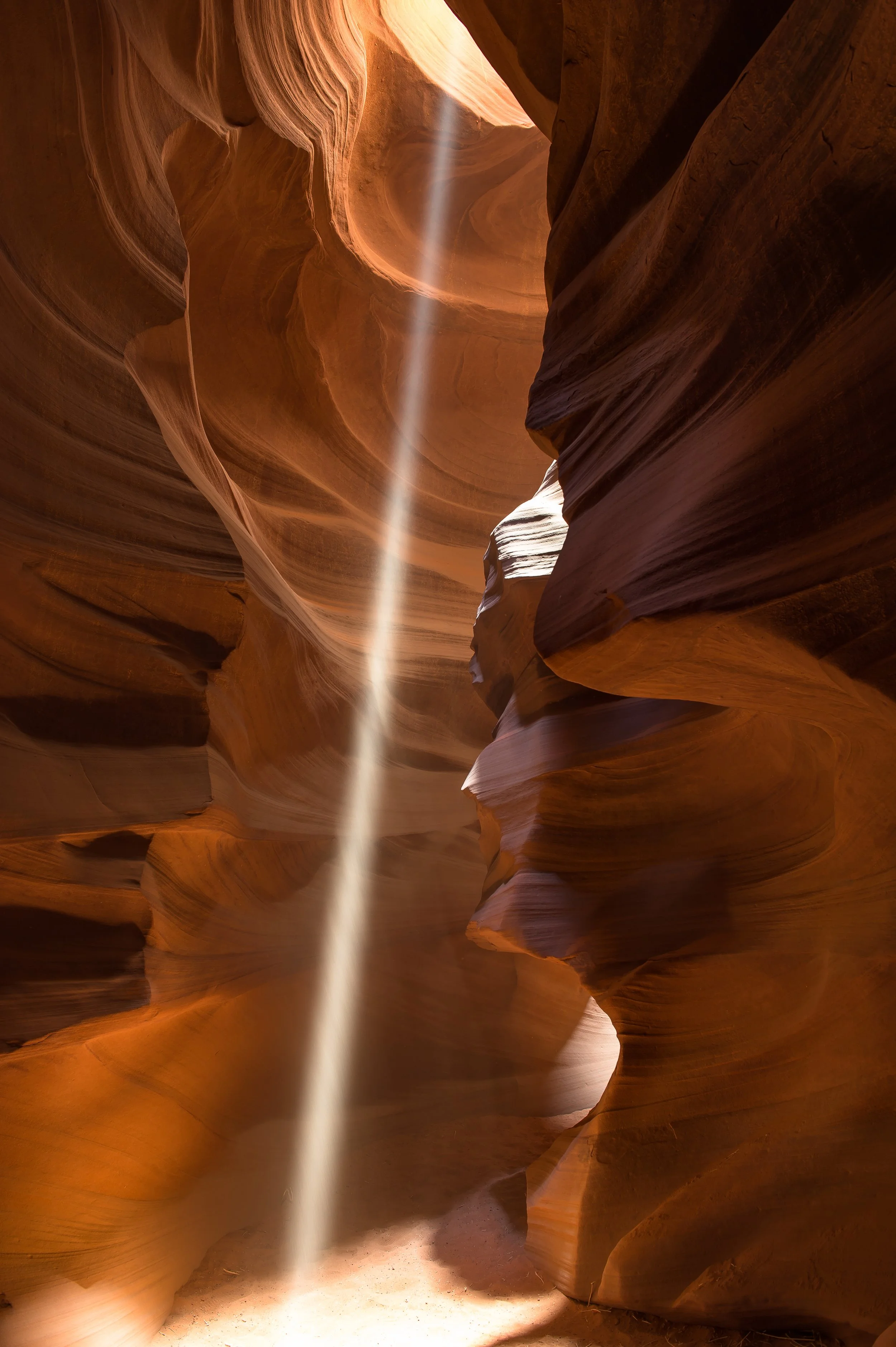 A striking moment of light shining down from the heavens in Antelope Canyon. The photo is taken from a low angle, looking upwards at the stunning rock formations that make up the canyon's walls. A beam of light shines down from the sky above, illumin