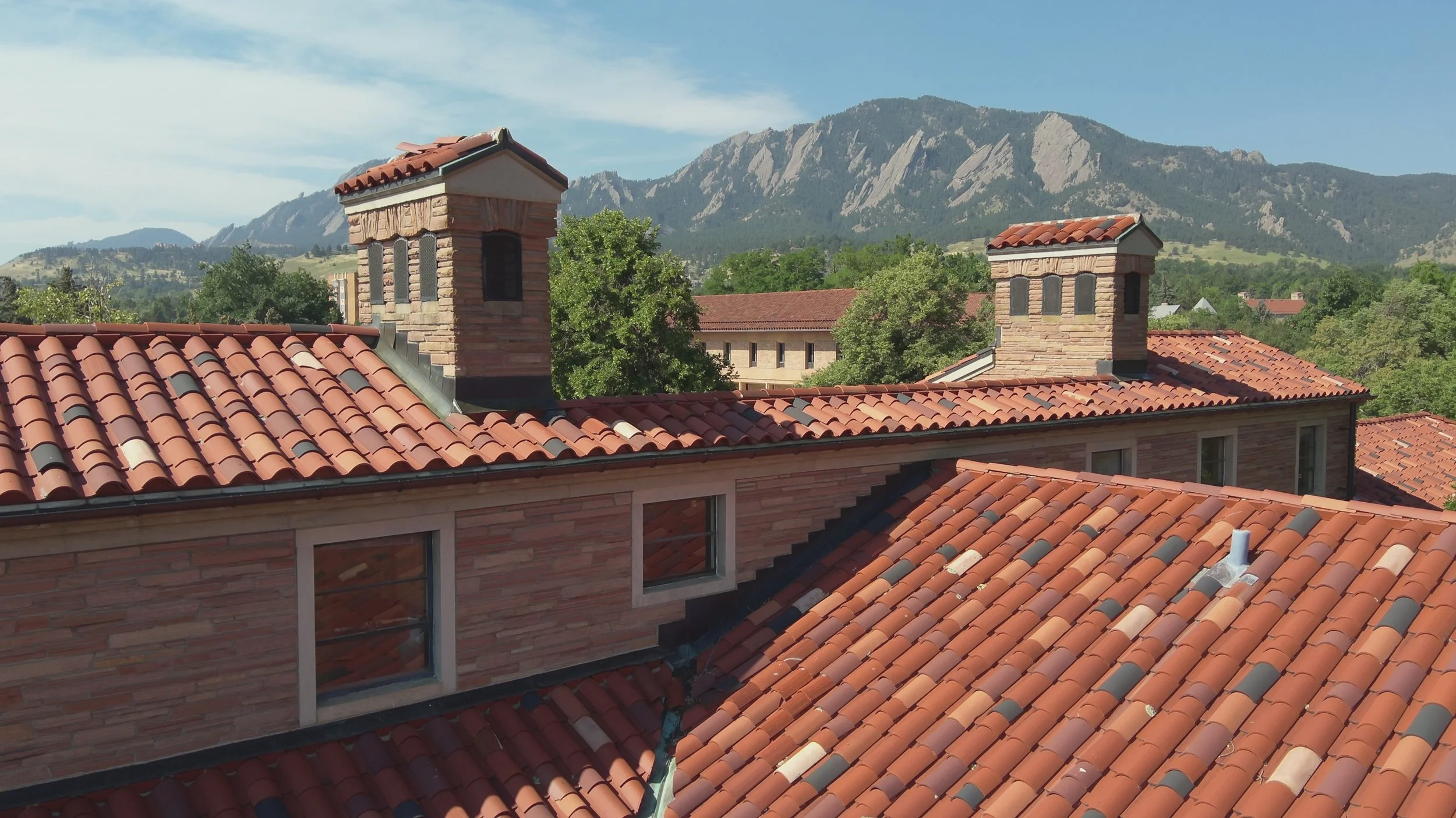 View of rooftops with red tile roofing, brick chimneys, and a mountain range in the background.