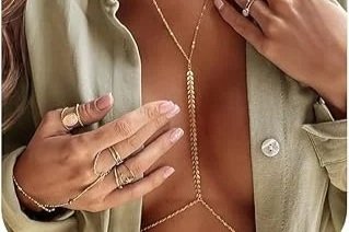 Close-up of a woman's chest and hands, showing layered necklaces and multiple rings on fingers, with beige clothing.