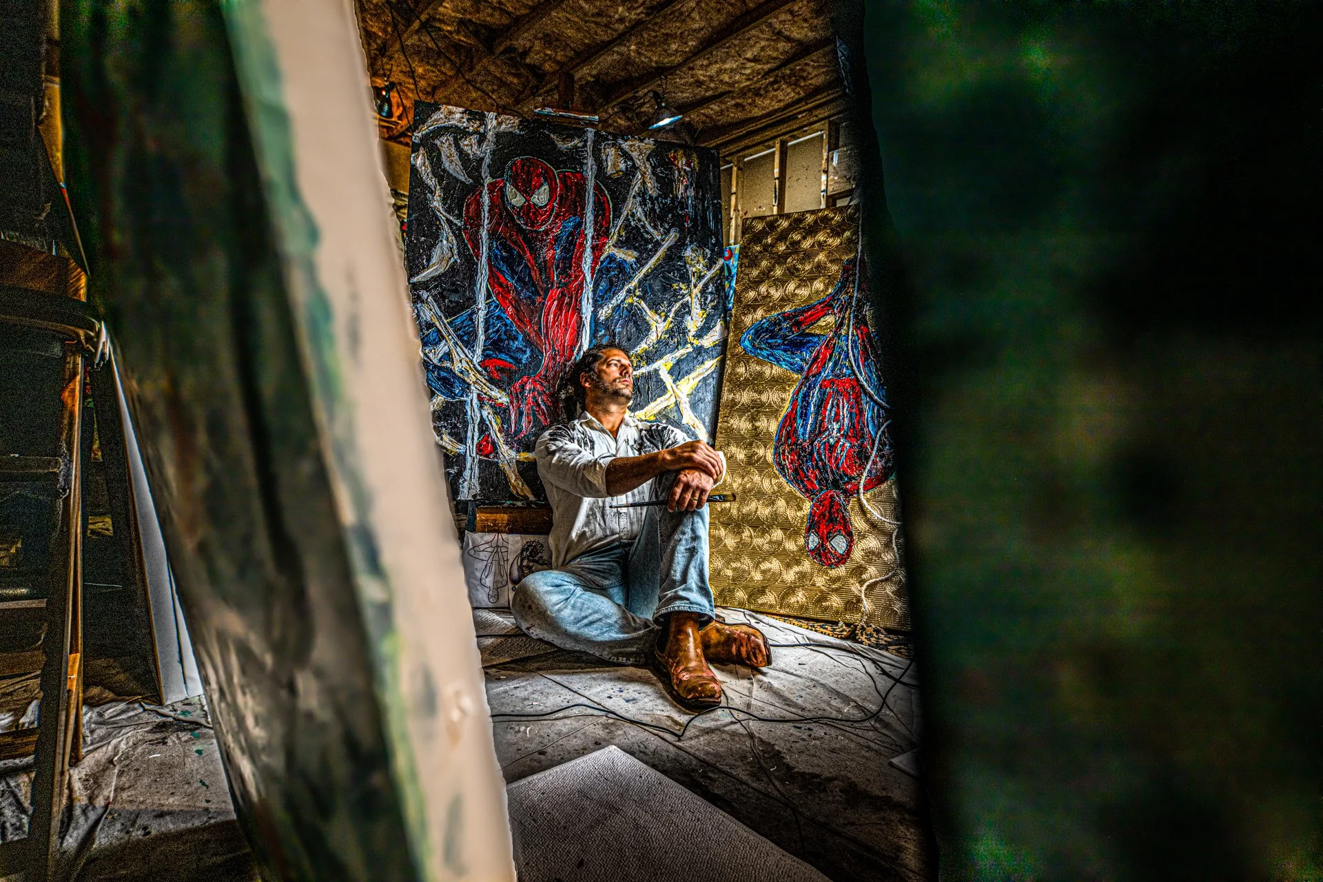 a fine art image of An artist sitting on the floor in front of colorful, Spider-Man-themed artwork in a studio.