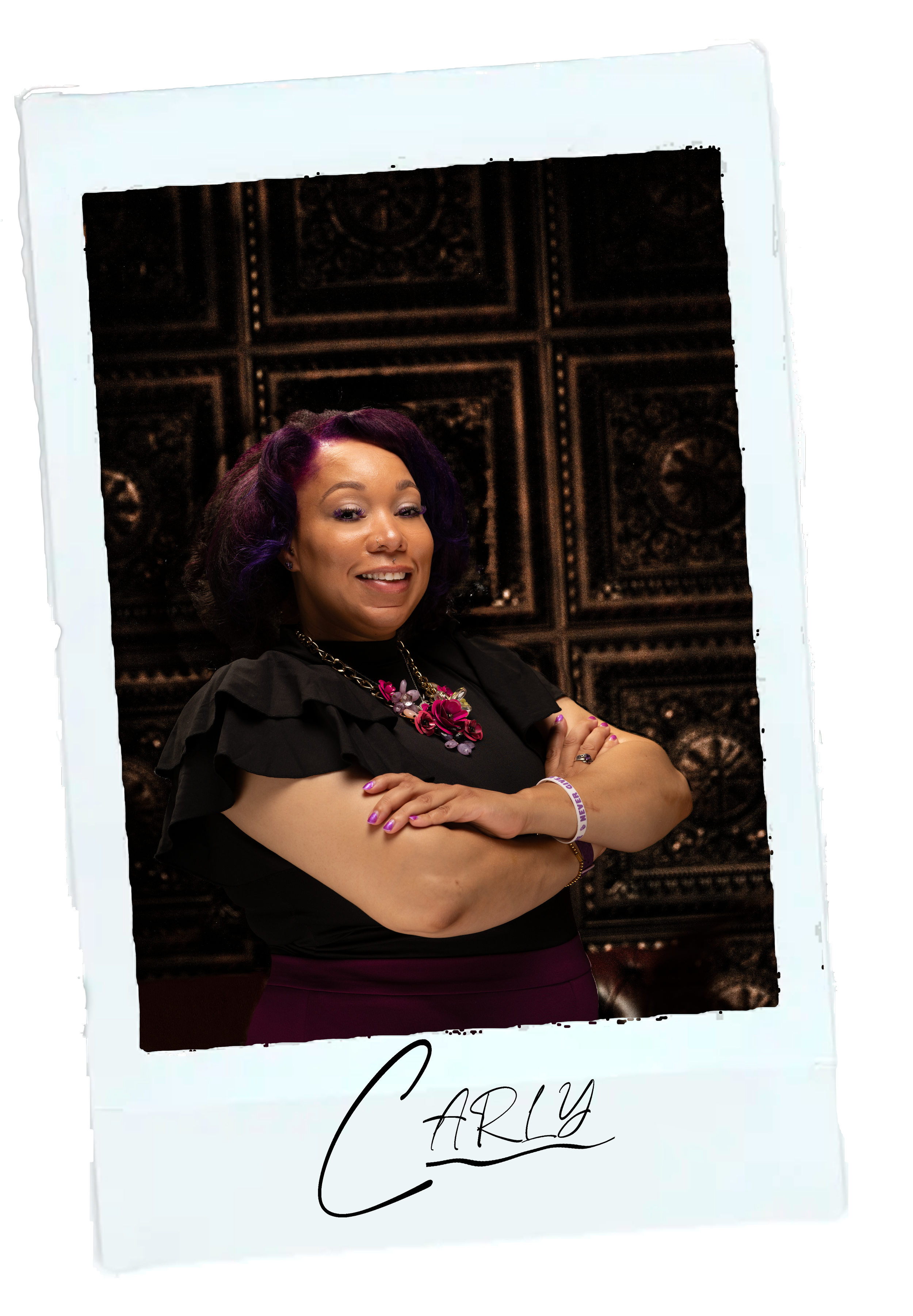 our makeup artist carly smiling, crossing her arms, wearing jewelry including a large necklace and ring, standing in front of a decorative wooden ceiling. The photo appears to be printed on an instant photo with handwritten text at the bottom.