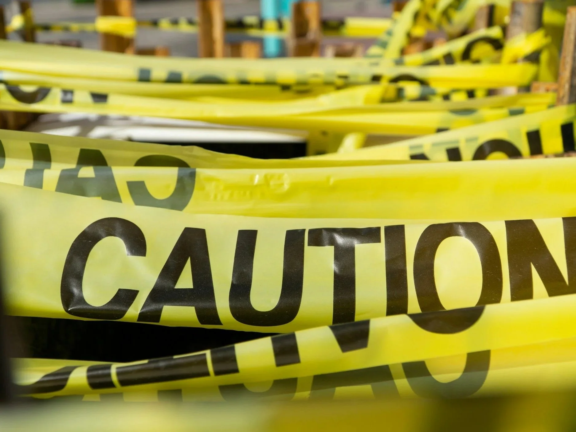 Multiple overlapping yellow caution tape with black text reading "CAUTION" on a storage shelf or warehouse.