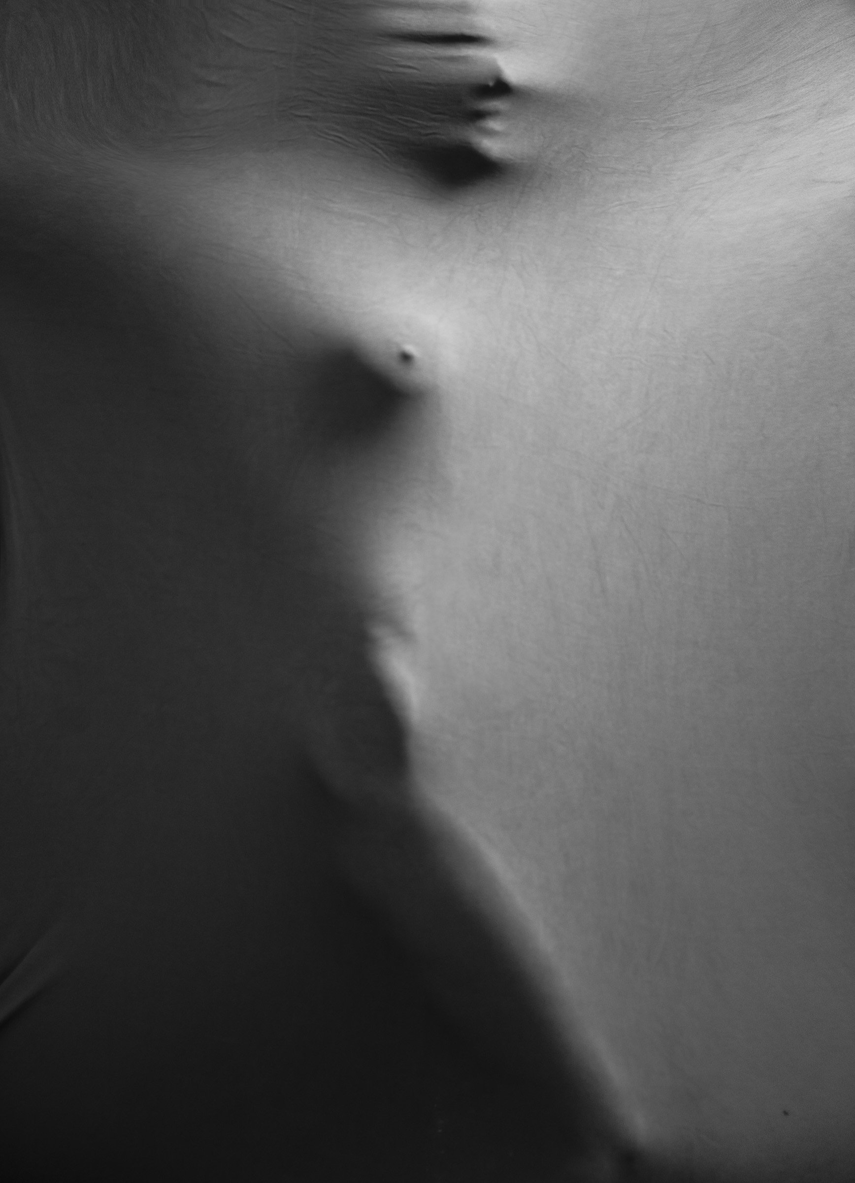 Close-up black and white photograph of a person's shoulder and neck, showing skin texture and a small mole or birthmark.