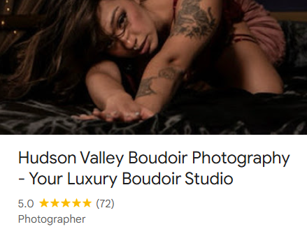 A woman with tattoos lying on a bed and reaching out toward the camera.