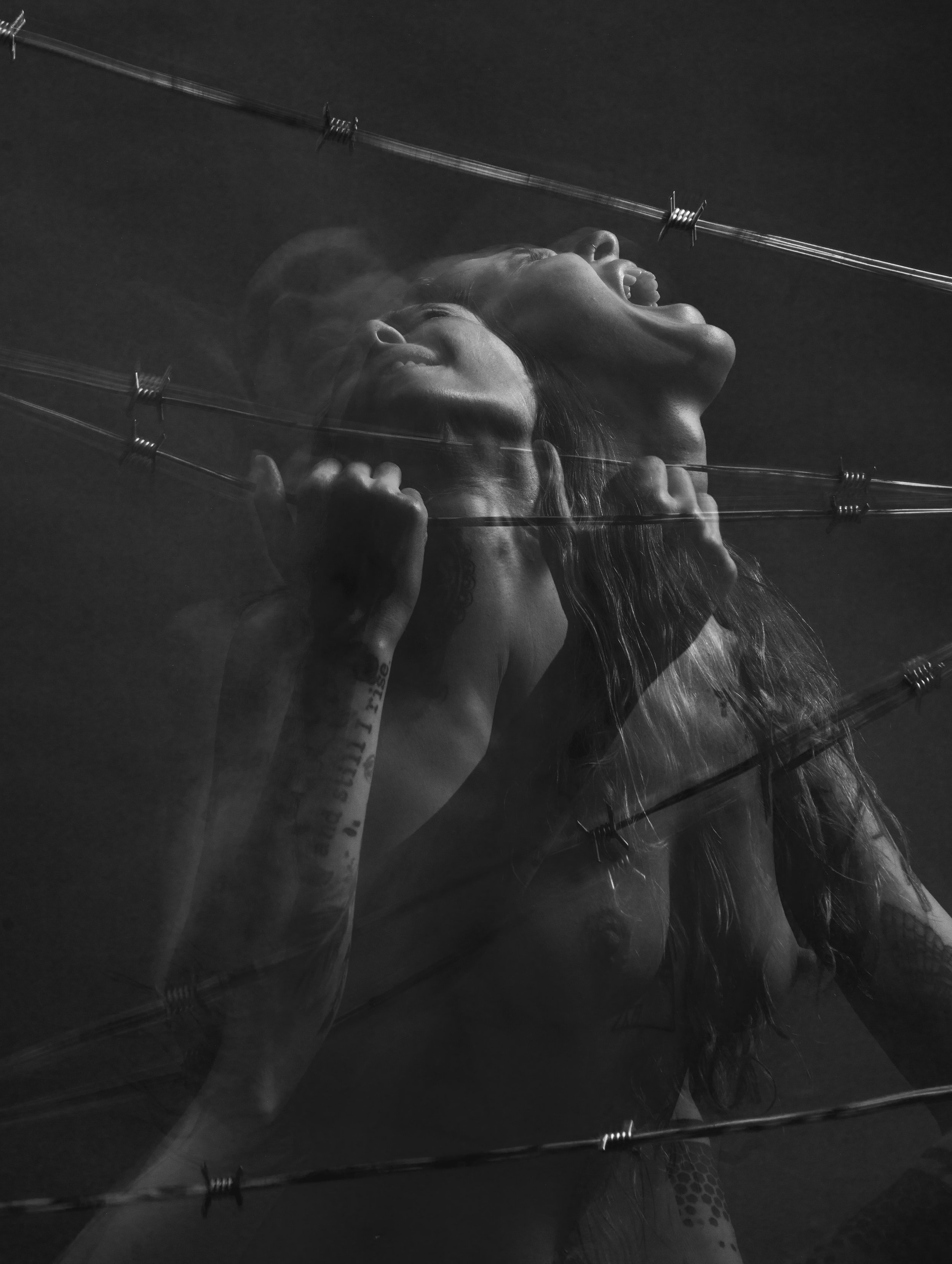 A black and white photo of a woman with long hair, she's holding her head with her hands, shouting or screaming, with a close-up view of her face. The image appears to be reflected or duplicated, creating a surreal or artistic effect.