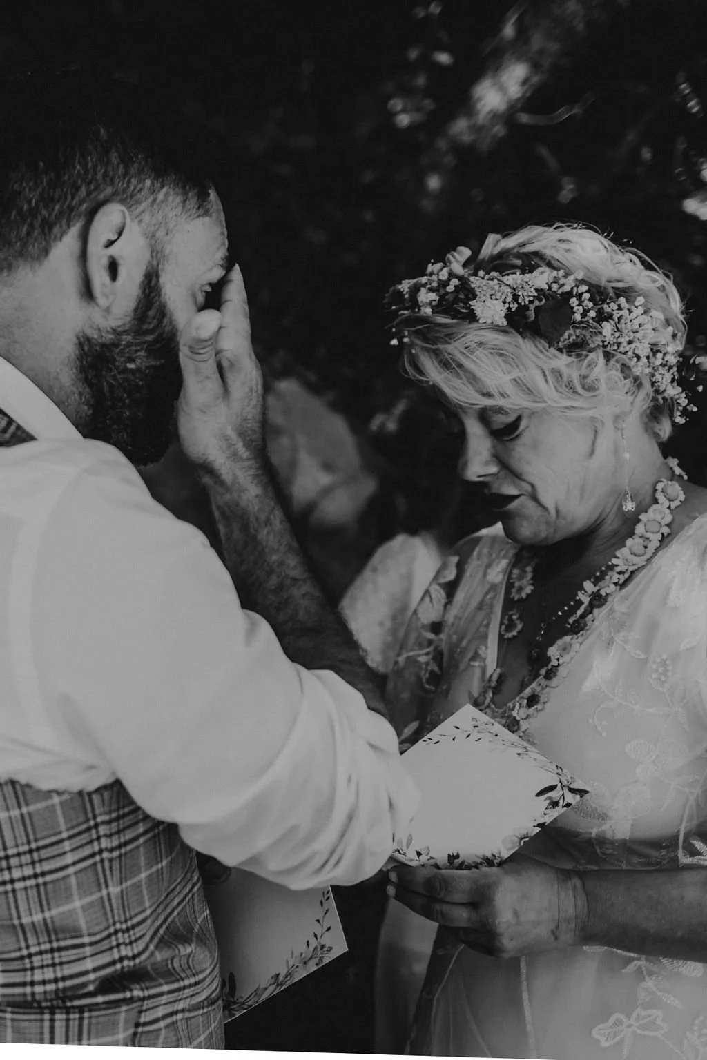 Casal no momento de uma troca de votos, com expressão emotiva, a mulher vestida com roupas tradicionais e coroa de flores, e o homem com barba e cabelo curtinho, em cenário de celebração.