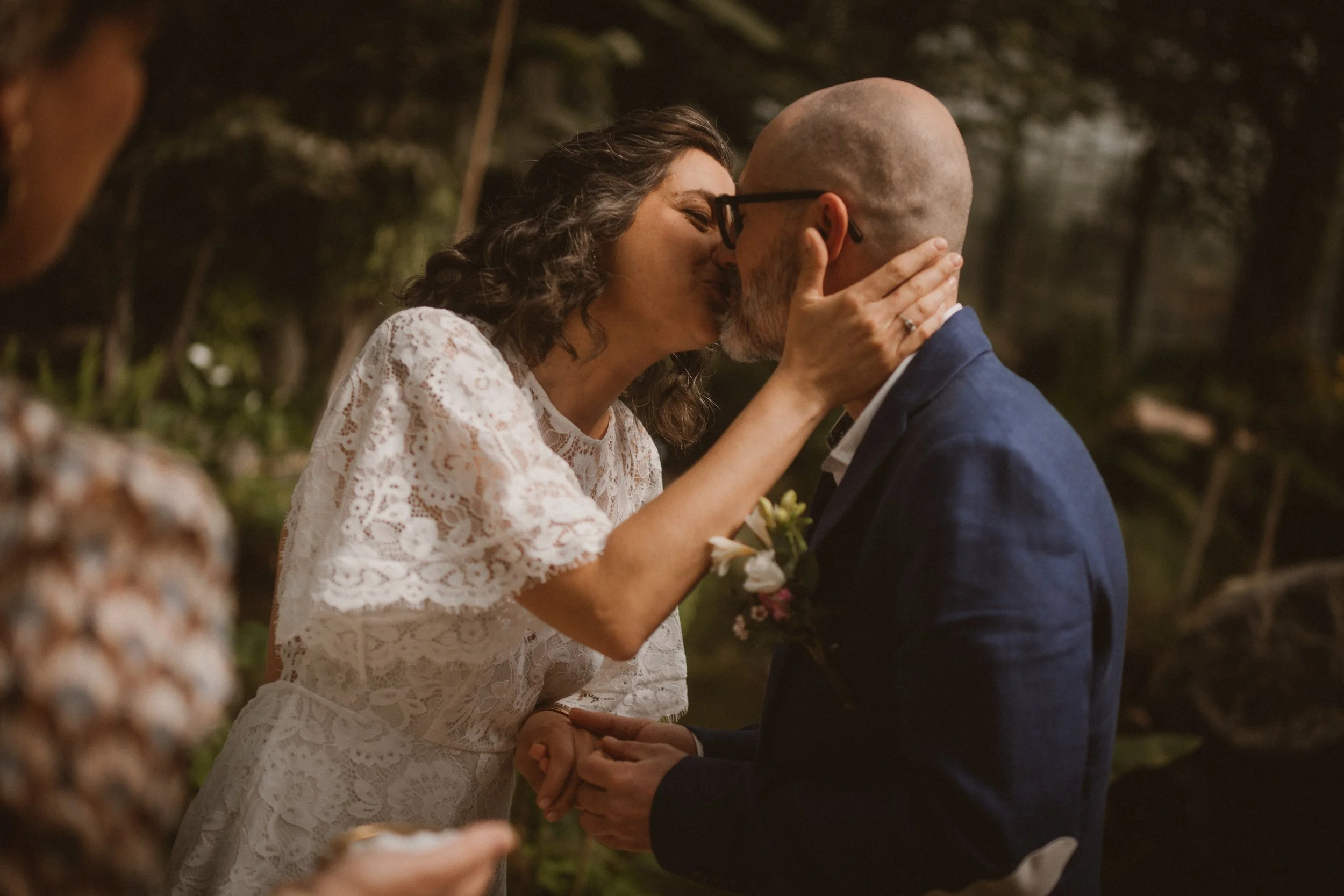 Casal de casamento trocando juras de amor ao ar livre durante a noite, com árvores ao fundo.