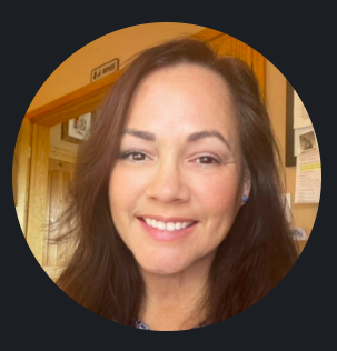 Smiling woman with long dark hair in indoor setting, wearing a blue top.