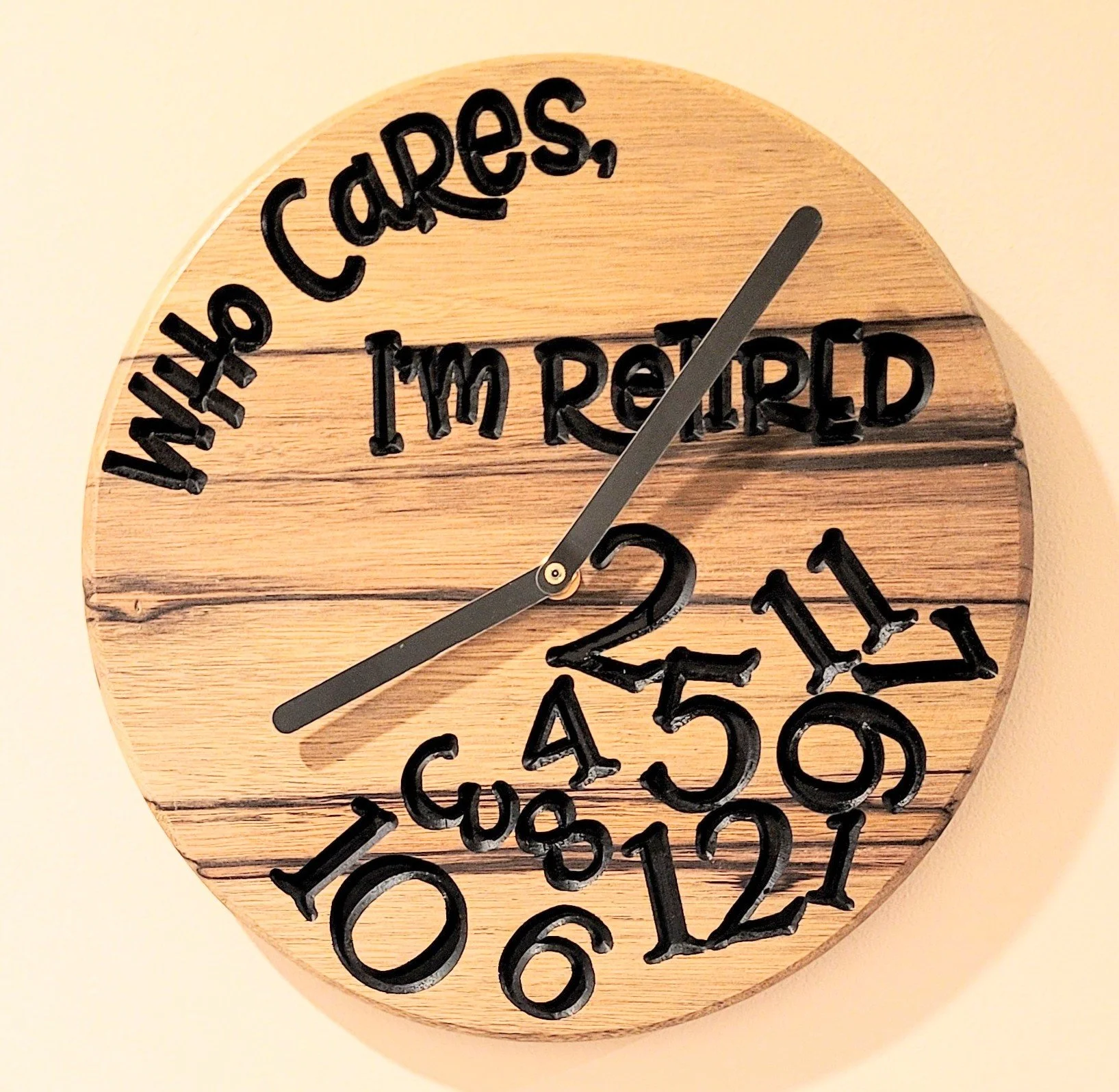 Wooden clock with black engraved numbers and text reading 'Who Cares, I'm Retired' and black clock hands.